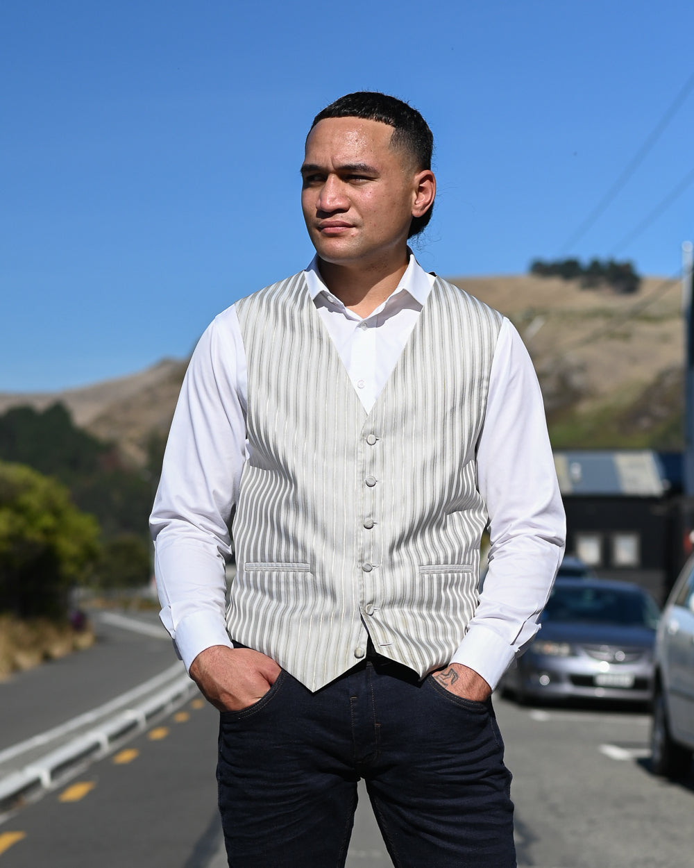 Handsome young man standing in the roadway wearing striped grey waistcoat and a white shirt