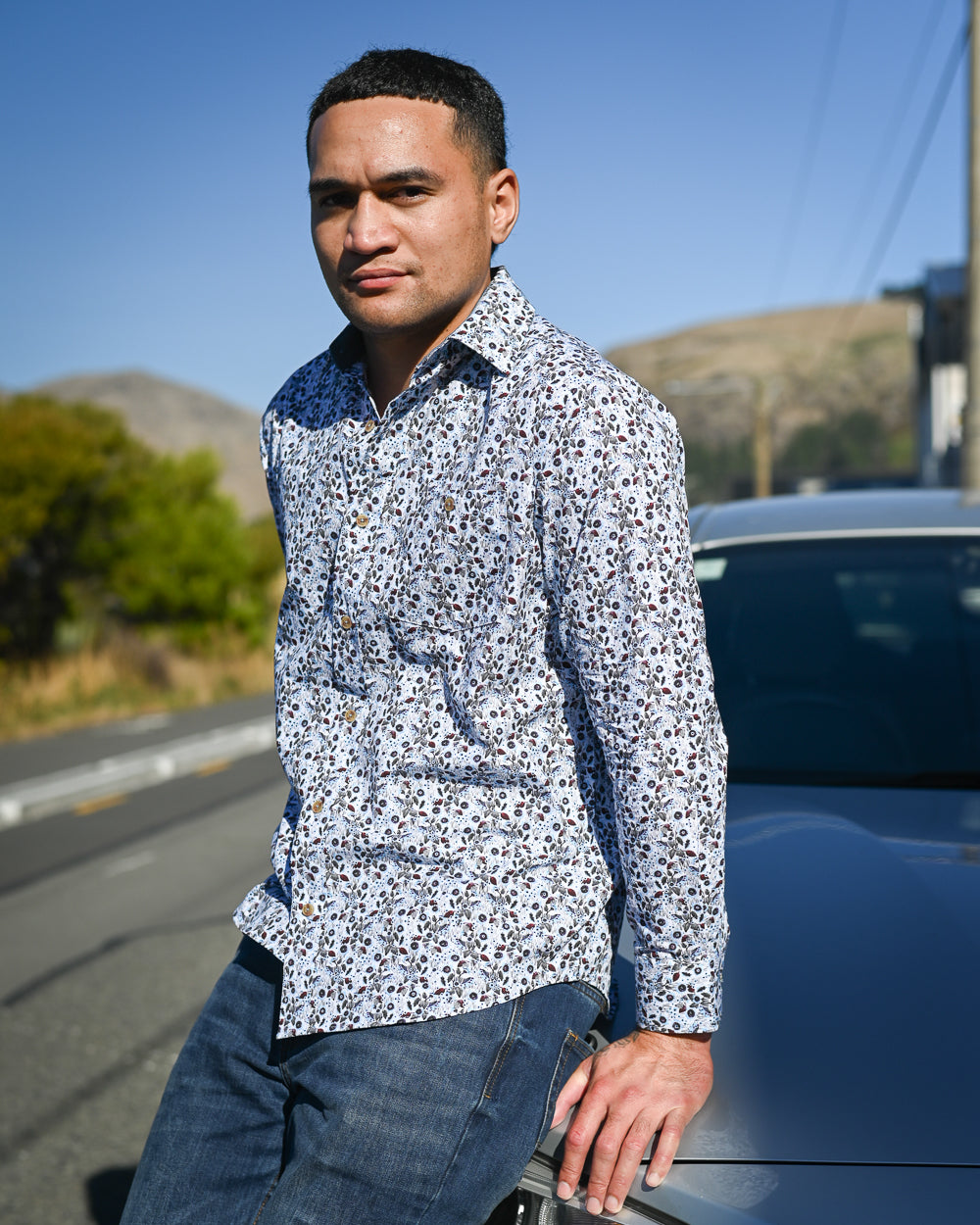 Handsome young man sitting on car bonnet wearing long-sleeve floral shirt