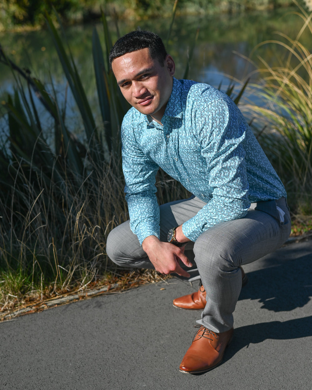 Handsome young Samoan man wearing turquoise shirt by Berlin and grey trousers by a river