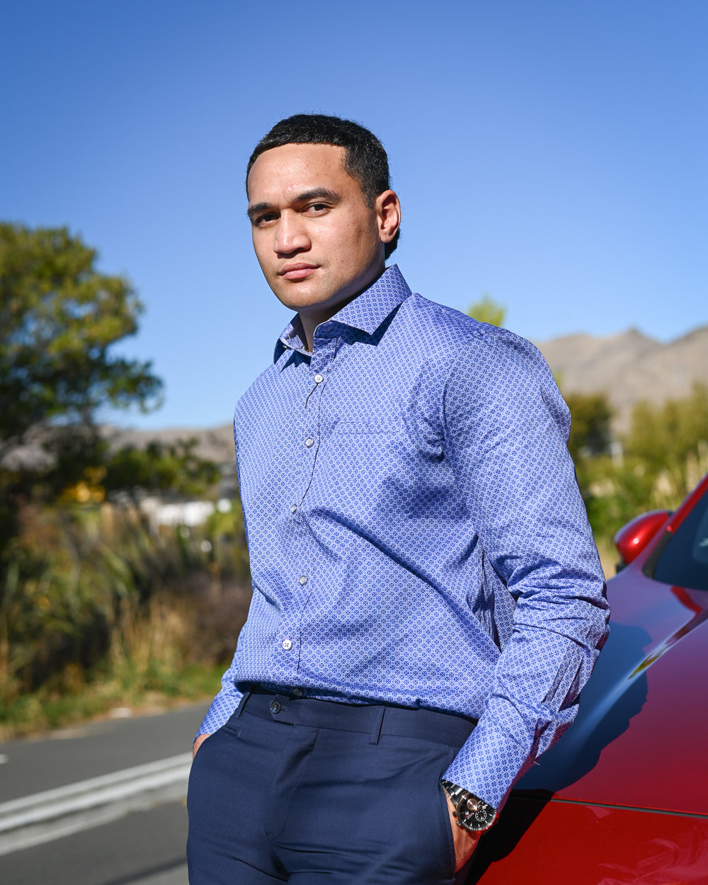 Handsome young Samoan man in sky-blue shirt by Berlin leaning on red car