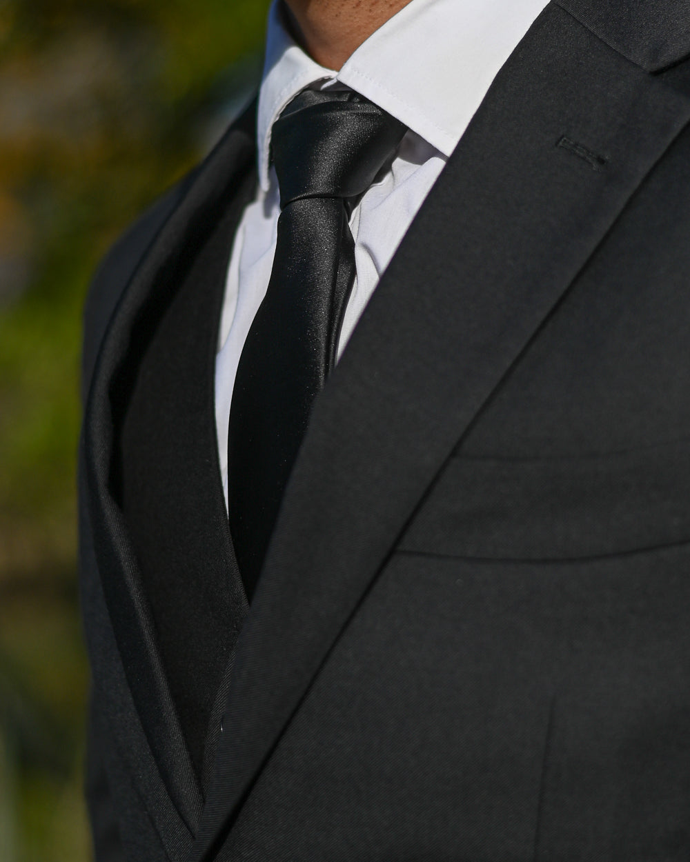 Black silk-look tie worn with a black three-piece suit