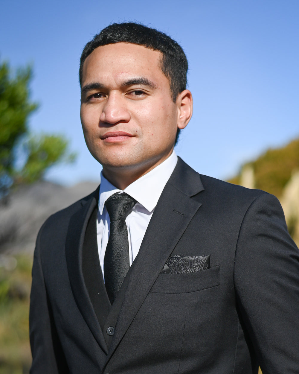 Young man in a three-piece black suit with a black paisley tie and matching pocket square