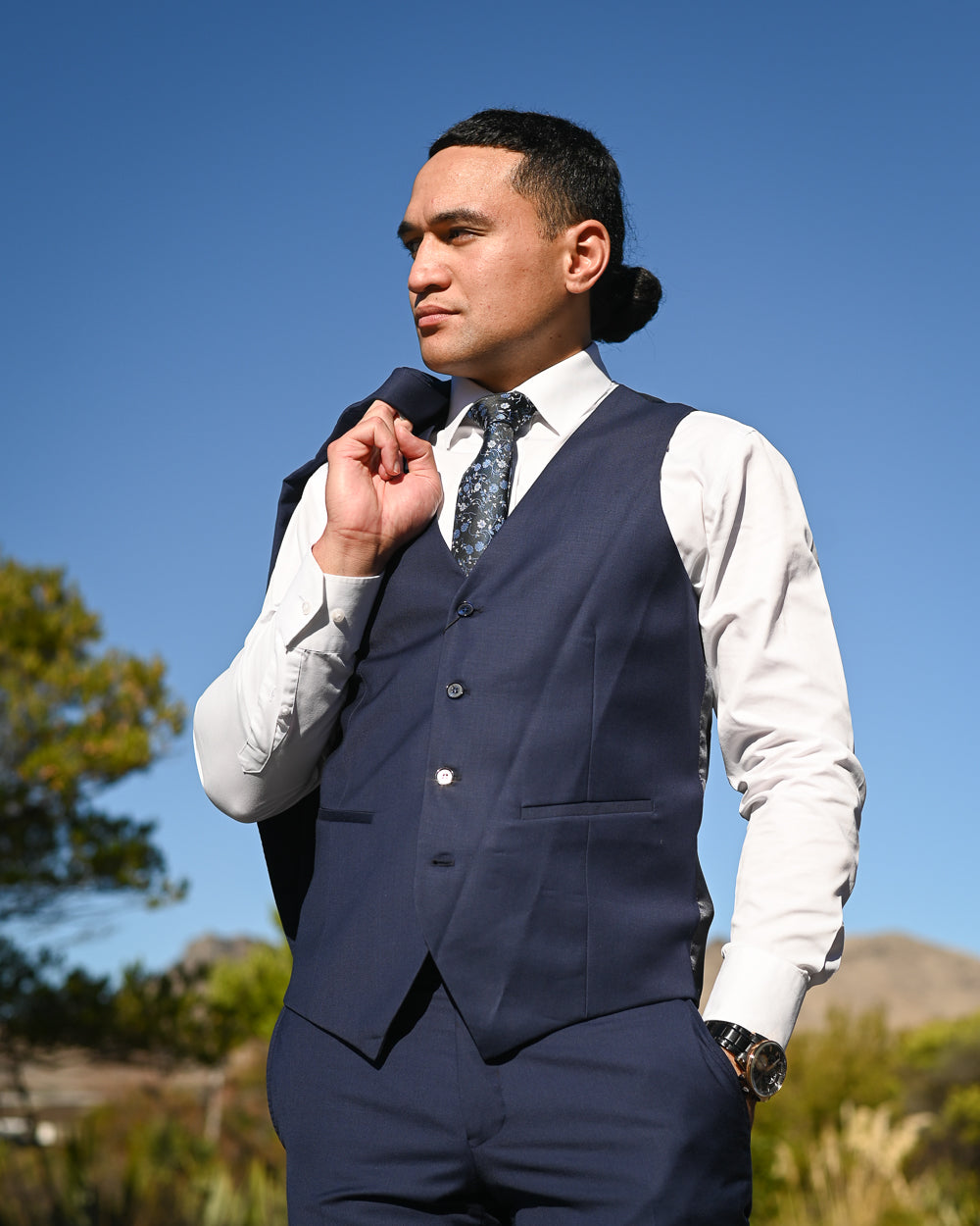 Young man in navy blue waistcoat and suit trousers with white shirt & blue tie